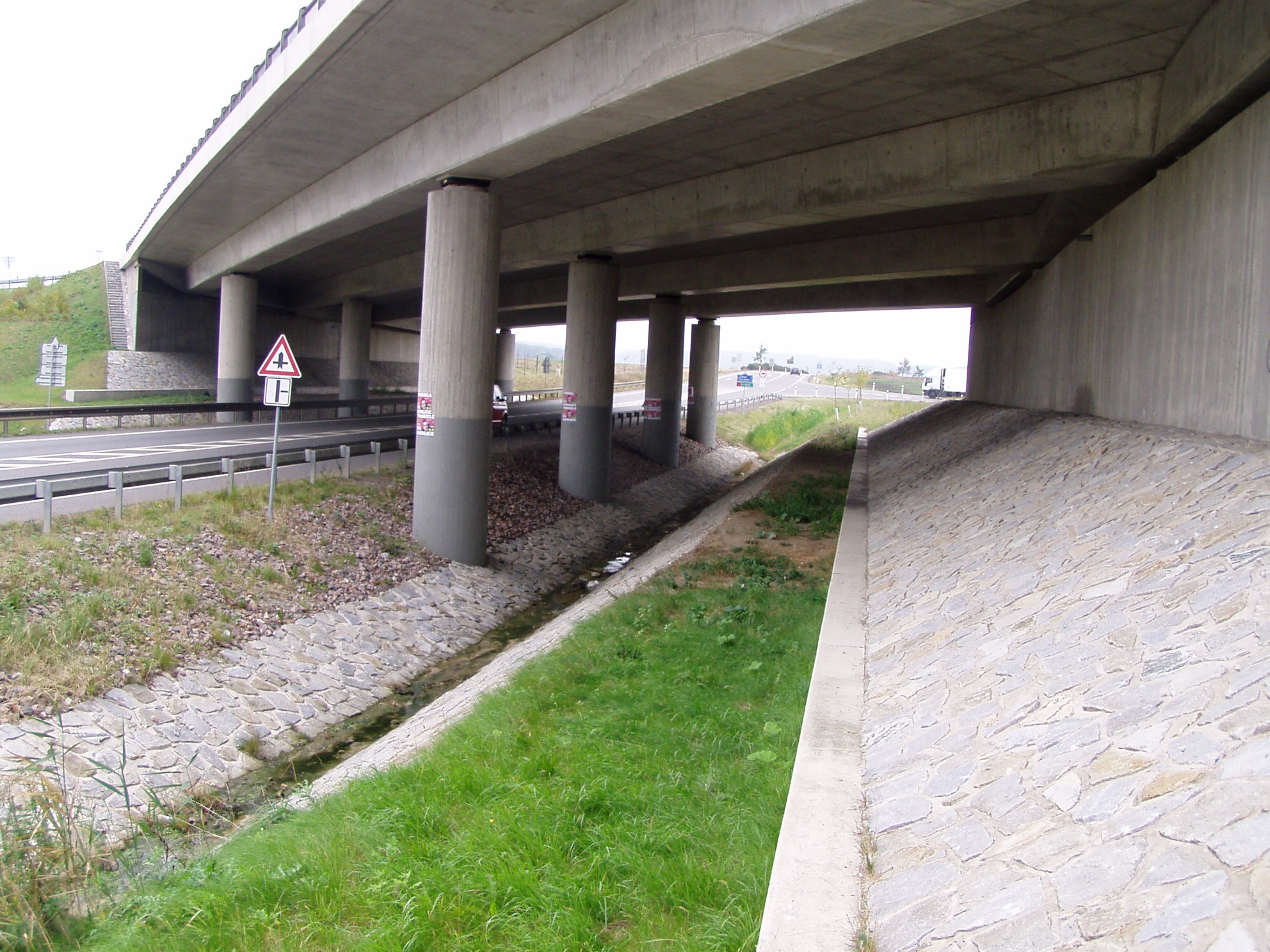 Obr. 7 a 8. Vlevo na fotografii je speciálně navržený migrační objekt na dálnici D11. Vpravo je konvenční most na D11 přes silnici první třídy I/36.  Zejména díky vytvoření pásu s přírodním povrchem, je tento most na exitu 36 prokazatelně využíván např. srncem, zajícem nebo liškou.  Foto Vlastimil Bogdan